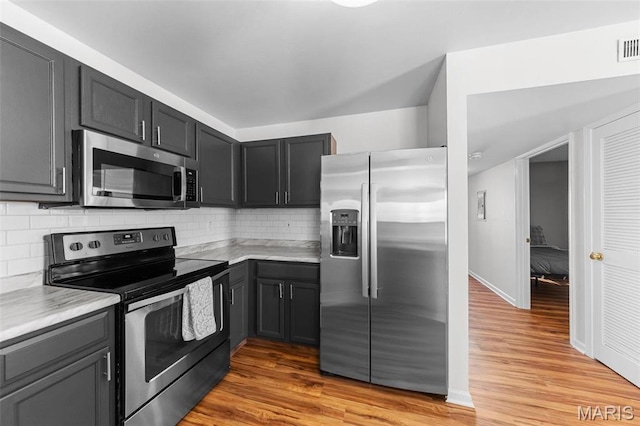 kitchen with appliances with stainless steel finishes, light countertops, light wood-type flooring, and decorative backsplash