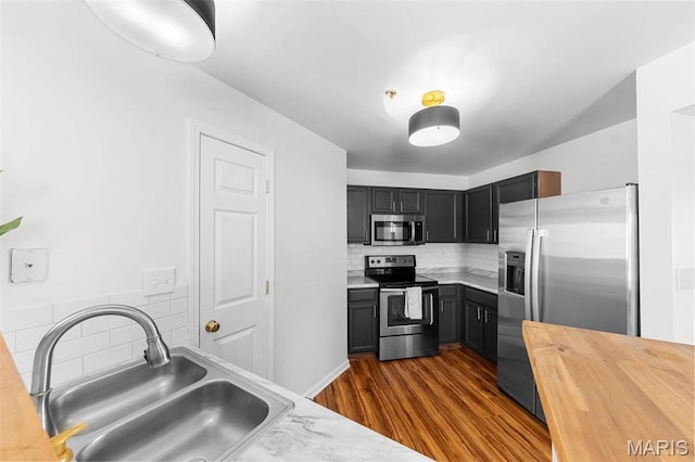 kitchen featuring appliances with stainless steel finishes, a sink, butcher block counters, dark wood-type flooring, and decorative backsplash