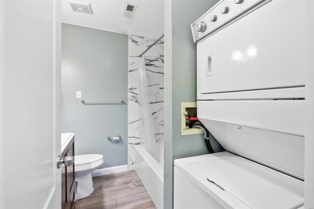 1052 S Kingshighway Blvd, Saint Louis, MO 63110 - full bathroom featuring stacked washer and clothes dryer, toilet, wood finished floors, shower / bathtub combination with curtain, and baseboards
