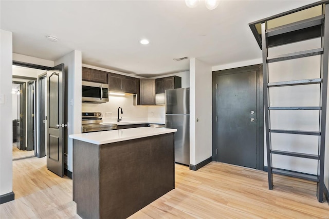 1052 S Kingshighway Blvd, Saint Louis, MO 63110 - kitchen with stainless steel appliances, dark brown cabinetry, light countertops, light wood-type flooring, and a kitchen island
