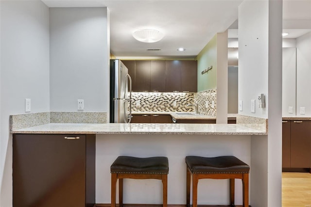1052 S Kingshighway Blvd, Saint Louis, MO 63110 - kitchen with freestanding refrigerator, a kitchen bar, tasteful backsplash, a peninsula, and dark brown cabinets