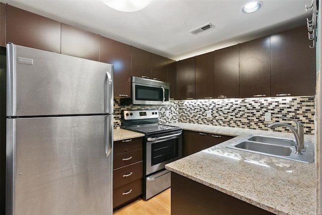 1052 S Kingshighway Blvd, Saint Louis, MO 63110 - kitchen with stainless steel appliances, a sink, dark brown cabinets, light wood-style flooring, and decorative backsplash
