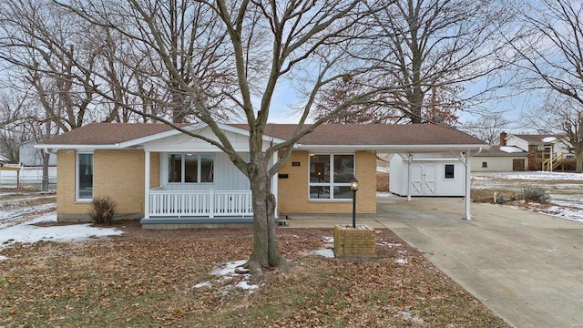 ranch-style home featuring covered porch, a storage unit, brick siding, concrete driveway, and an outbuilding