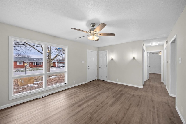 empty room with a ceiling fan, wood finished floors, baseboards, and a textured ceiling