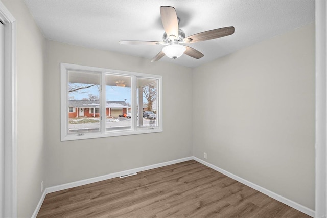 empty room with wood finished floors, a ceiling fan, and baseboards