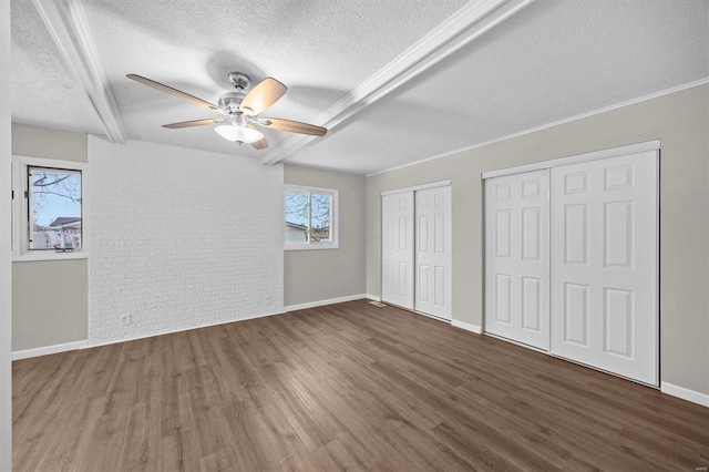 unfurnished bedroom featuring a textured ceiling, wood finished floors, multiple closets, baseboards, and beam ceiling
