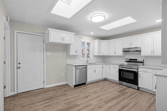 kitchen with stainless steel appliances, a skylight, a sink, light wood-style floors, and white cabinetry