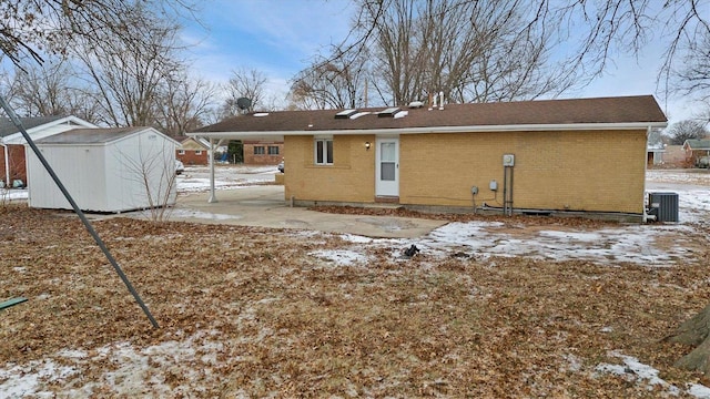 snow covered back of property featuring central AC unit, a storage shed, an outbuilding, and brick siding