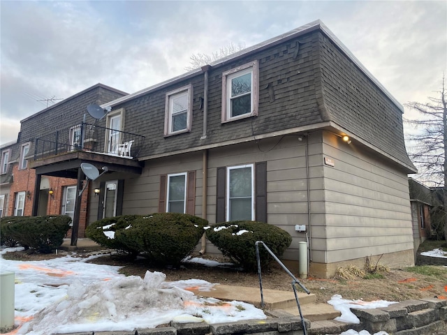 snow covered property featuring mansard roof, a shingled roof, and a balcony