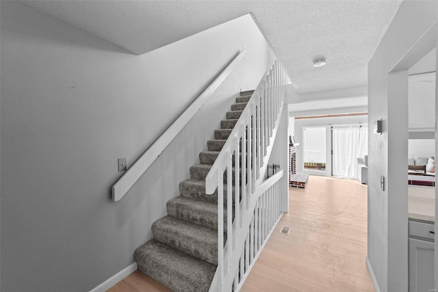 stairs with a textured ceiling, wood finished floors, and baseboards