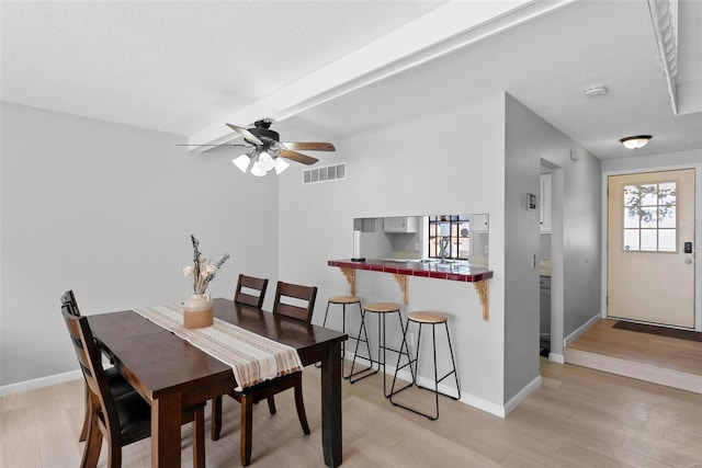 dining space featuring light wood finished floors, ceiling fan, baseboards, and beamed ceiling