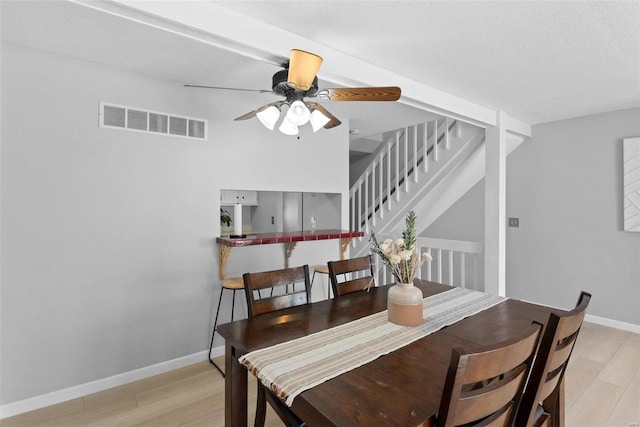 dining space with light wood-style flooring, ceiling fan, baseboards, and stairs