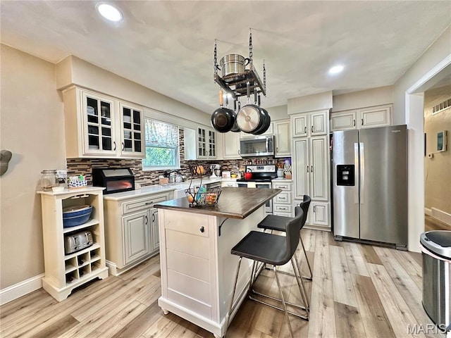 6 Ravenwood Cir, Ofallon, IL 62269 - kitchen featuring appliances with stainless steel finishes, a kitchen island, light wood finished floors, decorative backsplash, and glass insert cabinets