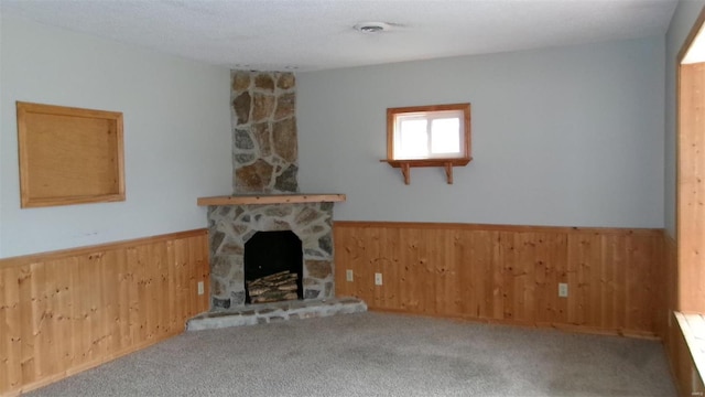 unfurnished living room with wooden walls, wainscoting, a stone fireplace, and carpet floors