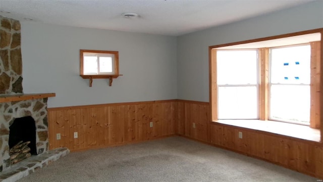 unfurnished living room with wainscoting, a fireplace, light carpet, and wood walls