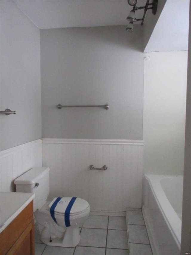 full bathroom featuring wainscoting, toilet, vanity, tile patterned flooring, and a bathtub