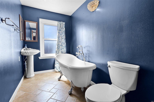 1317 Shenandoah Ave, Saint Louis, MO 63104 - bathroom with baseboards, toilet, a soaking tub, stone tile floors, and a sink