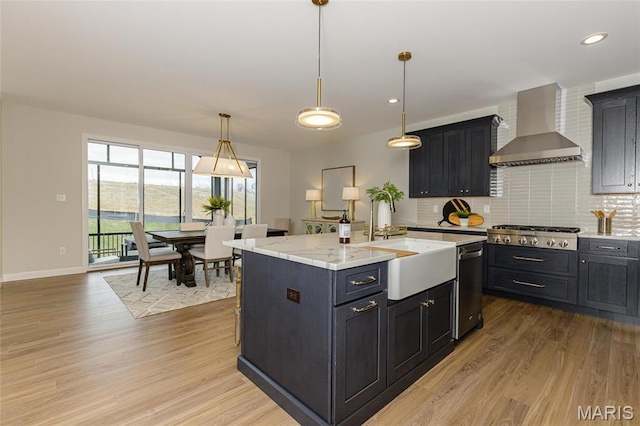212 Terradel Trl, Foristell, MO 63348 - kitchen with wall chimney range hood, stainless steel appliances, light wood-style floors, a sink, and an island with sink