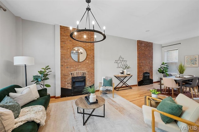 living area featuring a chandelier, wood finished floors, a brick fireplace, a wood stove, and baseboards