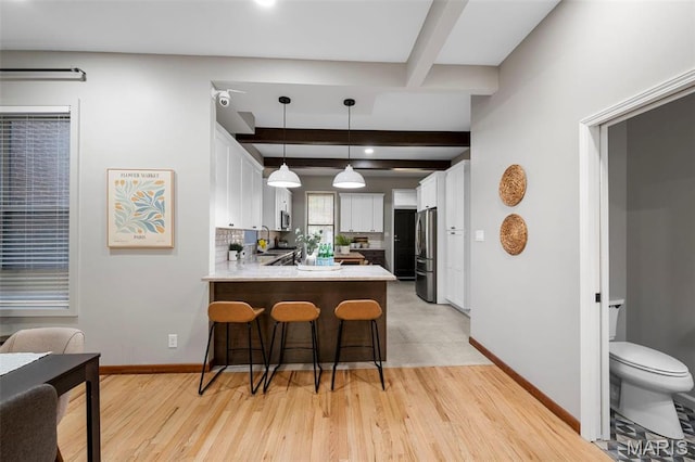 kitchen with a peninsula, freestanding refrigerator, beam ceiling, baseboards, and light wood-style flooring