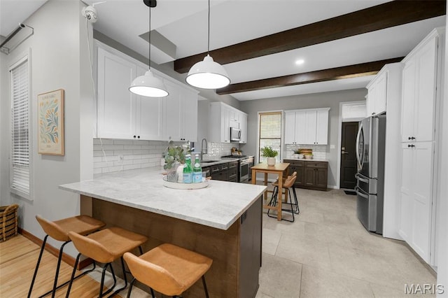 kitchen featuring appliances with stainless steel finishes, a peninsula, backsplash, a sink, and beamed ceiling