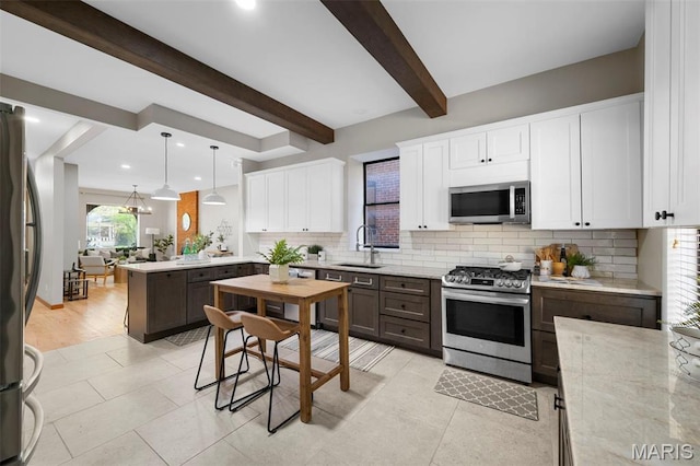 kitchen featuring appliances with stainless steel finishes, a peninsula, a sink, decorative backsplash, and beamed ceiling