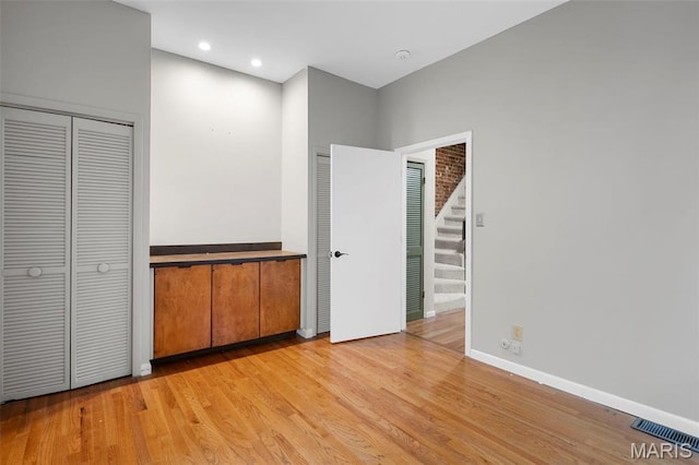 unfurnished bedroom with light wood finished floors, two closets, recessed lighting, and baseboards