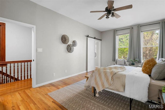bedroom featuring light wood-style floors, a barn door, baseboards, and a ceiling fan