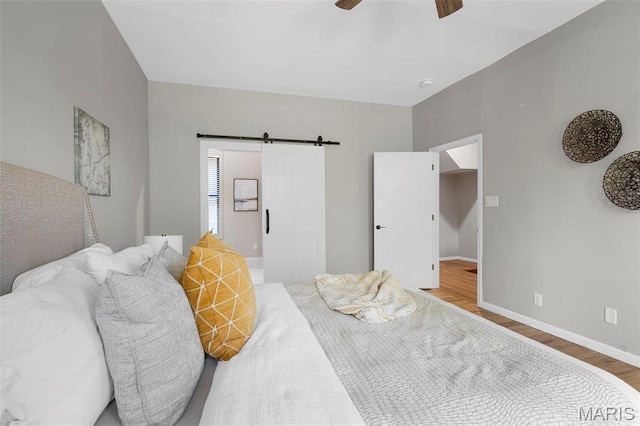 bedroom with wood finished floors, baseboards, a barn door, and ceiling fan