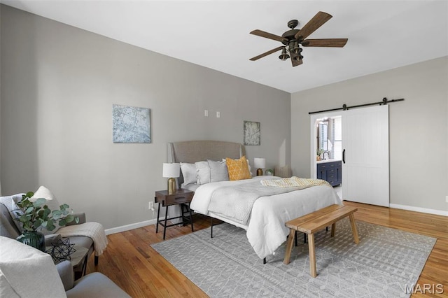 bedroom with baseboards, wood finished floors, a barn door, and a ceiling fan