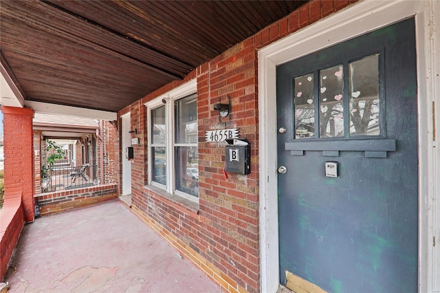 view of exterior entry featuring a porch and brick siding