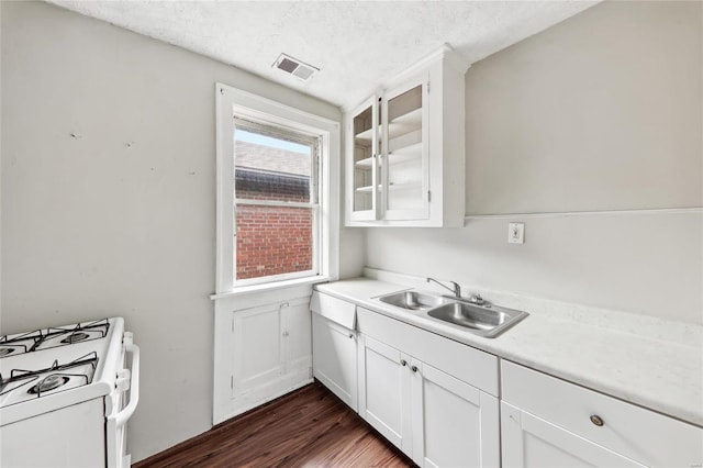 kitchen with white range with gas stovetop, a sink, dark wood finished floors, white cabinets, and light countertops