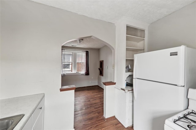kitchen featuring freestanding refrigerator, a textured ceiling, arched walkways, gas range oven, and wood finished floors
