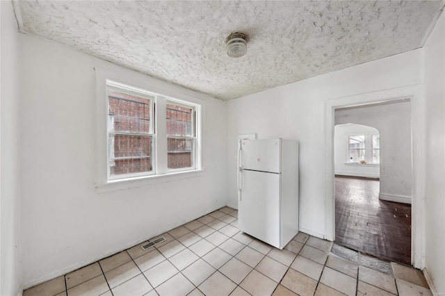 kitchen featuring freestanding refrigerator, light tile patterned flooring, a textured ceiling, and arched walkways
