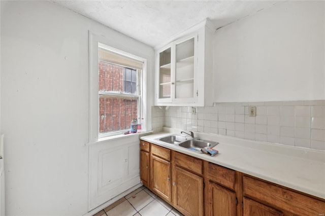kitchen with a sink, light tile patterned floors, light countertops, glass insert cabinets, and brown cabinets