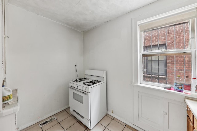 kitchen with gas range gas stove, light tile patterned floors, baseboards, and tile countertops