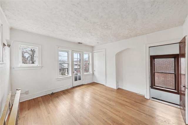 empty room with light wood-type flooring, arched walkways, baseboards, and a textured ceiling