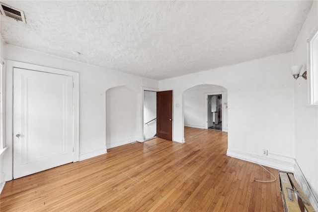 spare room featuring arched walkways, a textured ceiling, light wood-style flooring, and baseboards