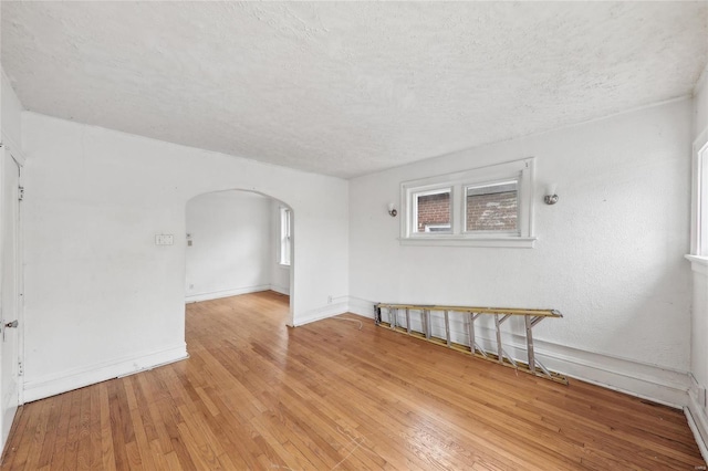 unfurnished room featuring arched walkways, light wood-style flooring, a textured ceiling, and baseboards