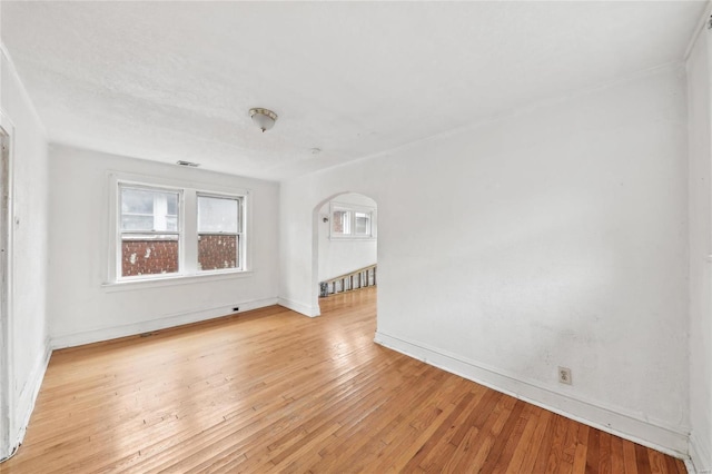 unfurnished room with arched walkways, baseboards, and light wood-style flooring