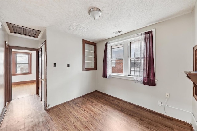 spare room featuring light wood-type flooring, baseboards, and a textured ceiling