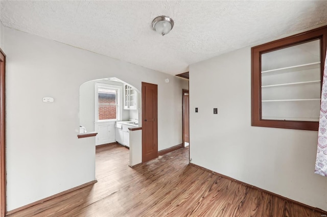 spare room featuring arched walkways, a textured ceiling, light wood-style floors, and baseboards