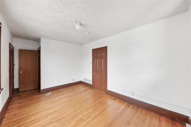 empty room with light wood-style floors, baseboards, and a textured ceiling