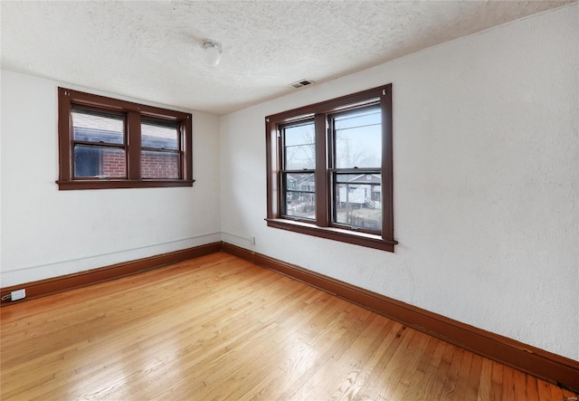 spare room featuring baseboards, light wood finished floors, and a textured ceiling