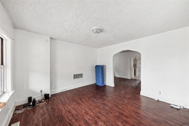 unfurnished room with wood finished floors, arched walkways, a textured ceiling, and baseboards