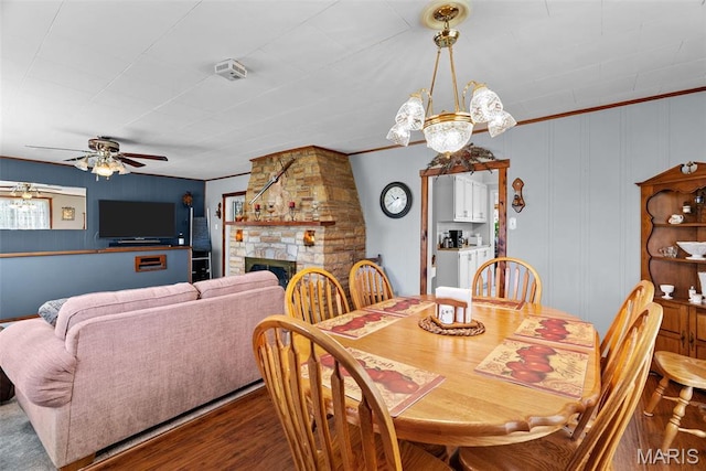 dining room with a ceiling fan, dark wood-style flooring, a fireplace, a chandelier, and crown molding