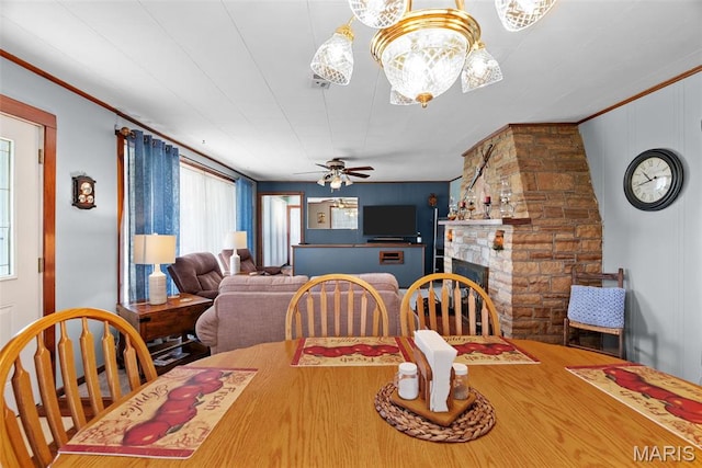dining room featuring ceiling fan, a stone fireplace, and crown molding