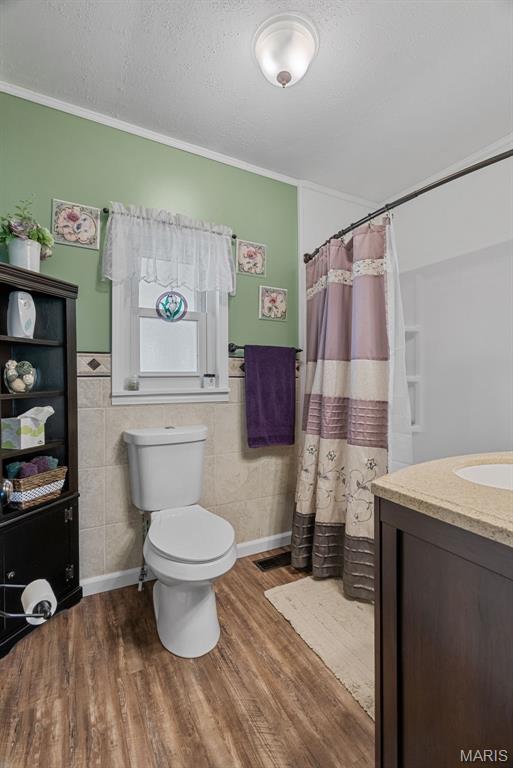 full bathroom featuring wood finished floors, toilet, vanity, curtained shower, and a wainscoted wall