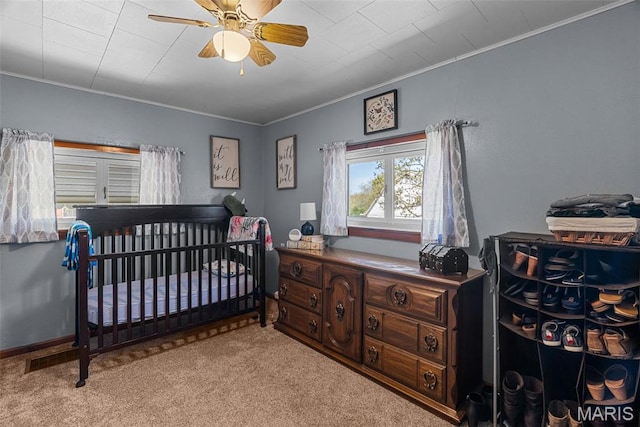 bedroom with crown molding, light colored carpet, ceiling fan, and a nursery area