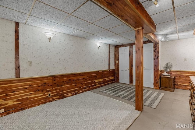 finished below grade area featuring a paneled ceiling, a wainscoted wall, wood walls, and wallpapered walls
